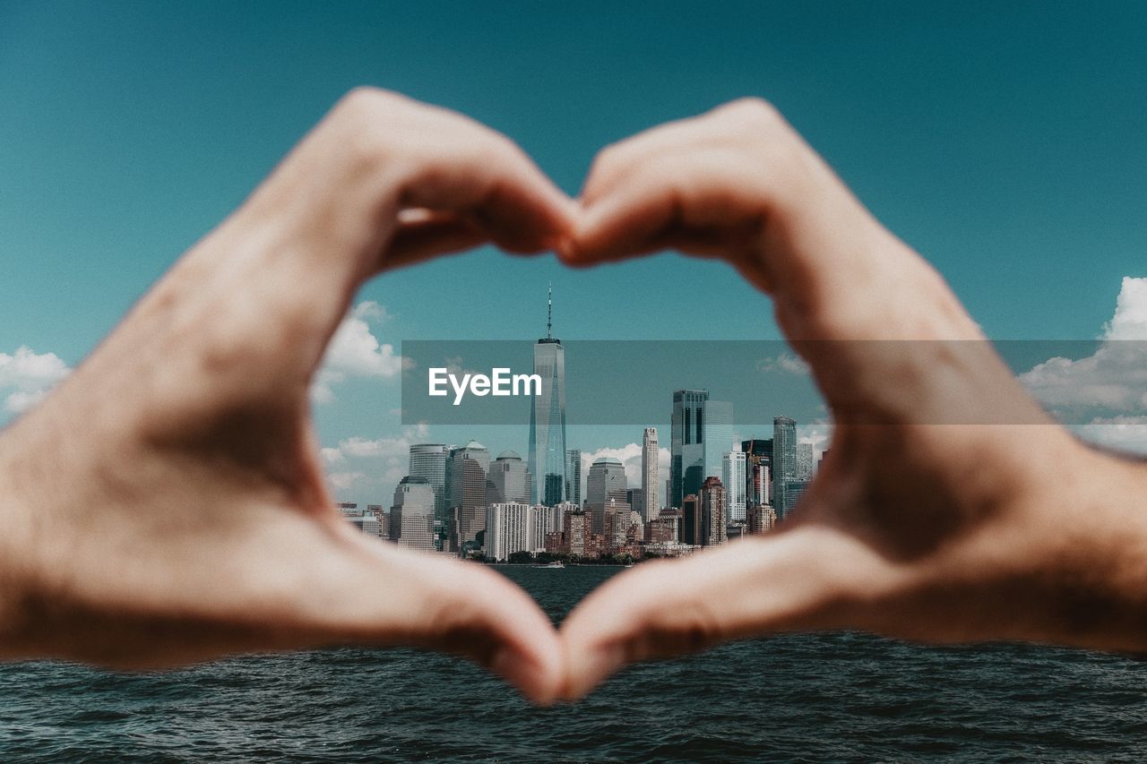 Close-up of hand making heart shape against building in city