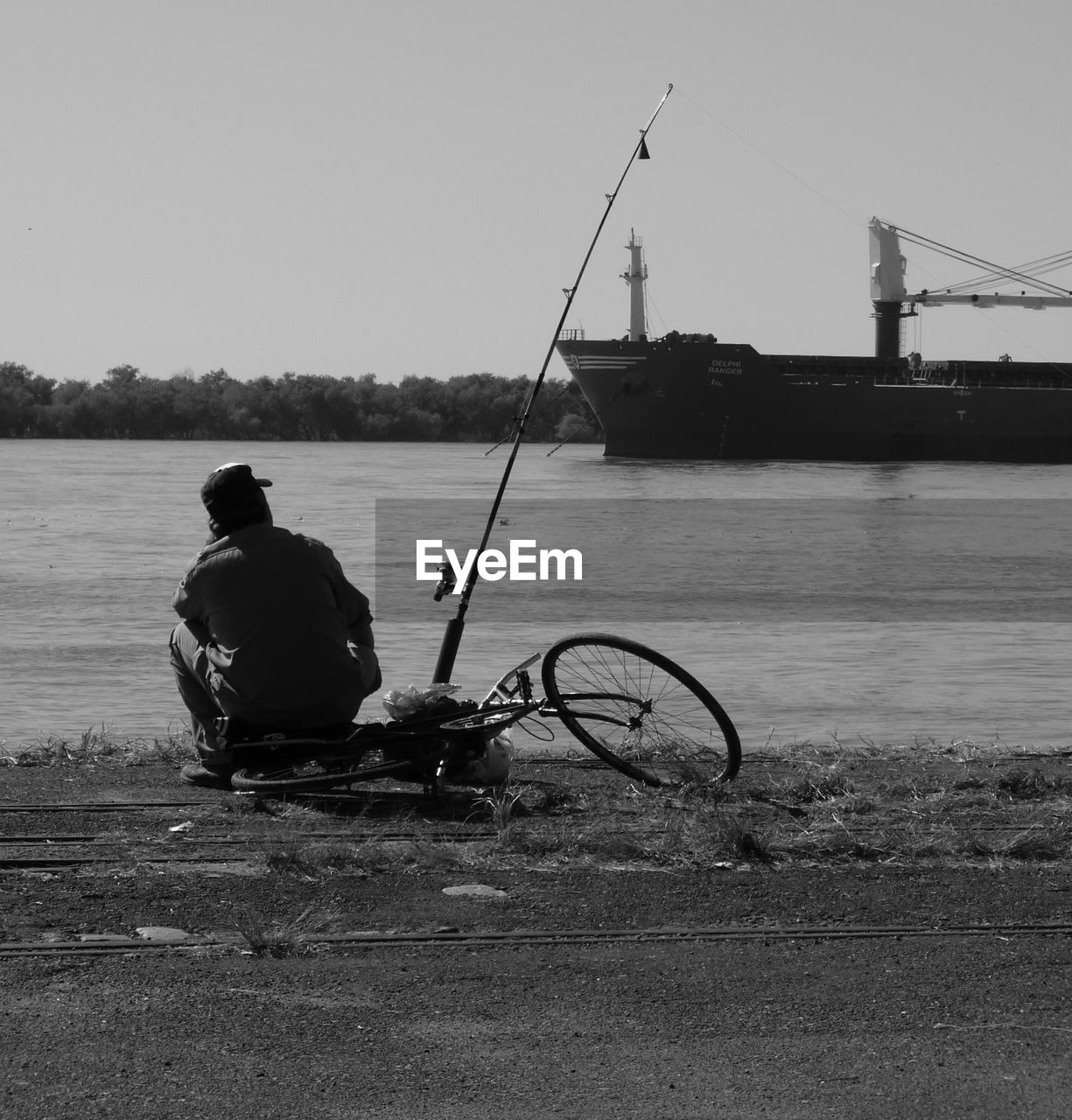 Rear view of man fishing at lake against sky