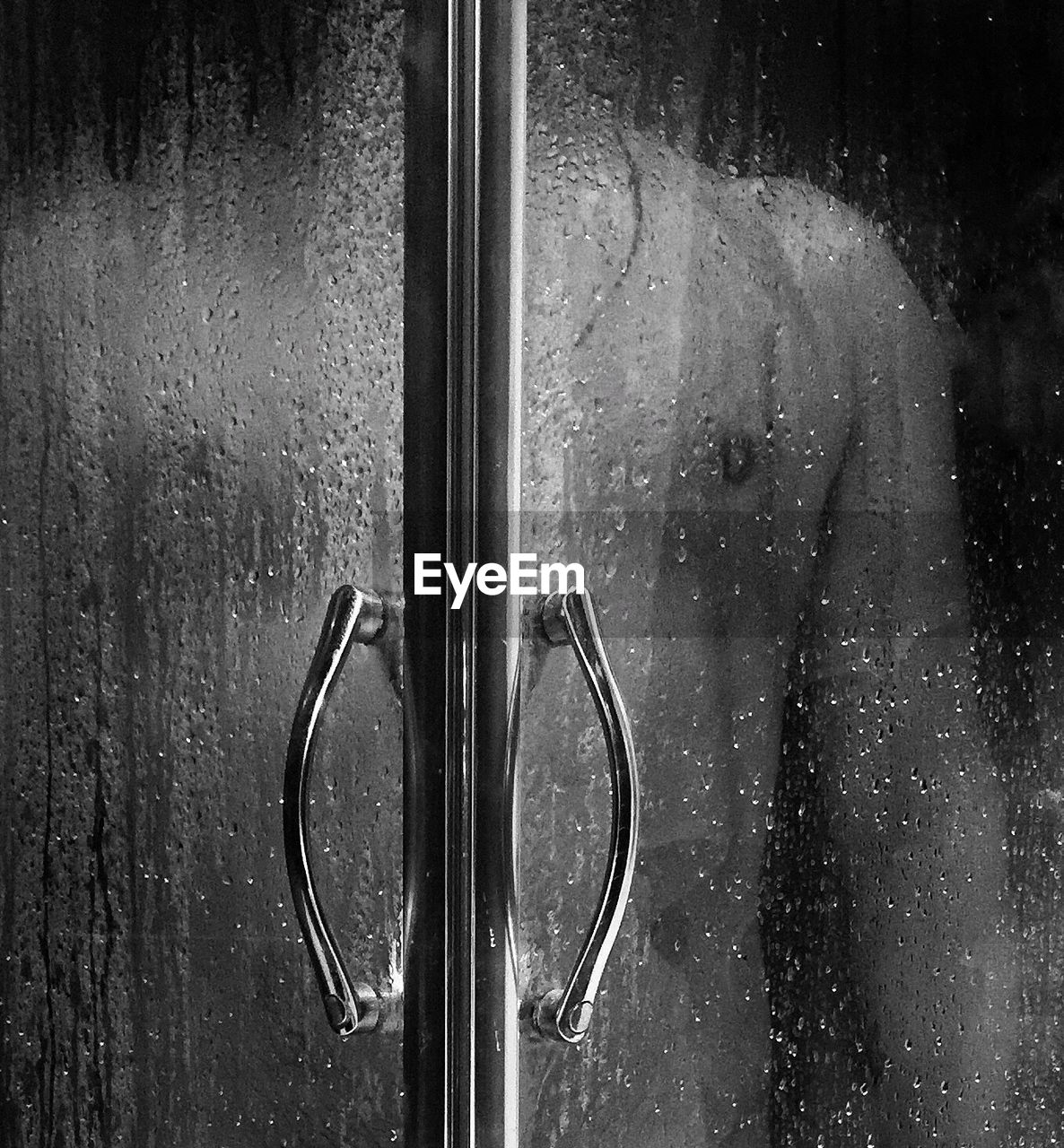 Midsection of shirtless man seen through wet glass door