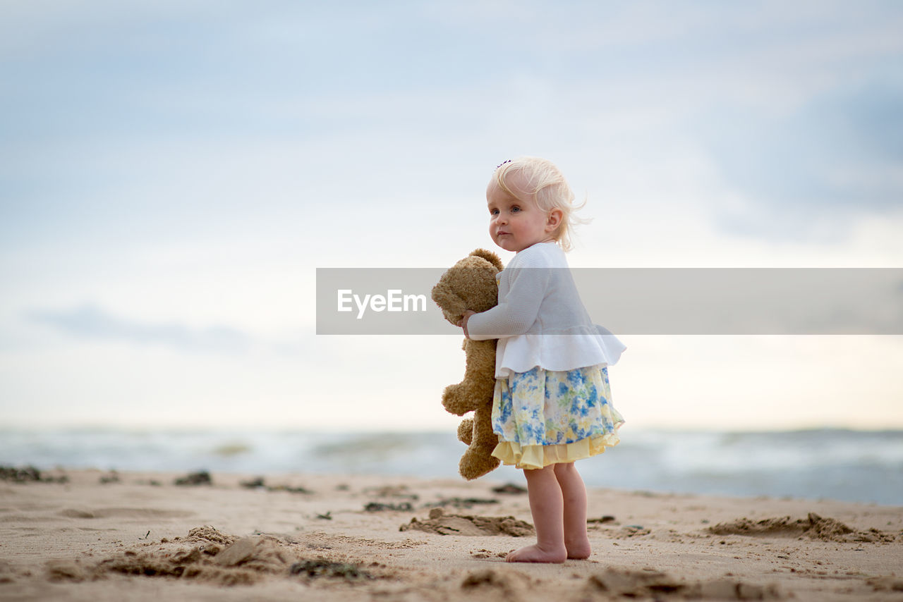 Girl with stuffed toy at beach against sky