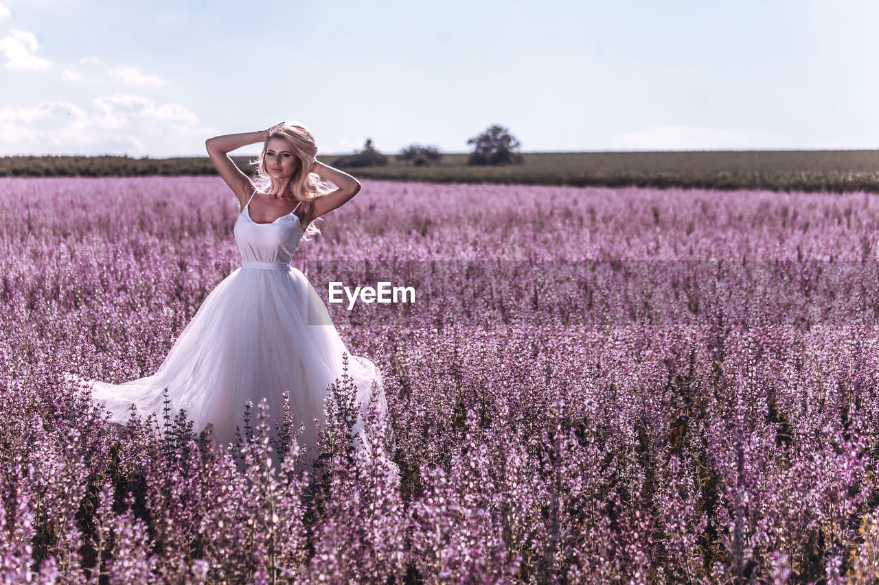 FULL LENGTH OF WOMAN STANDING ON FIELD WITH PURPLE FLOWERS