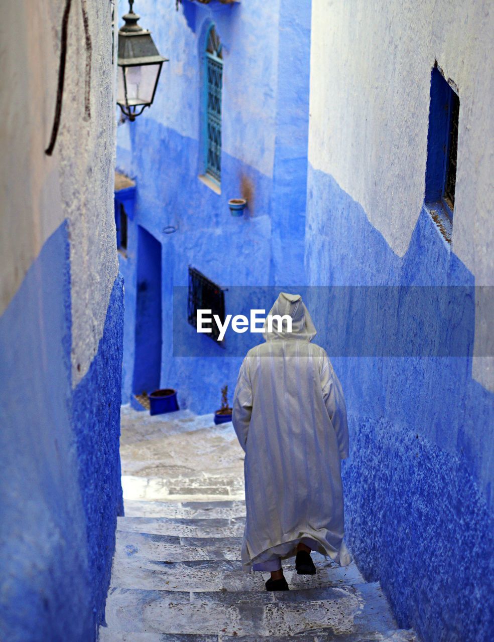 Moroccan man in hooded robe walks down the blue street