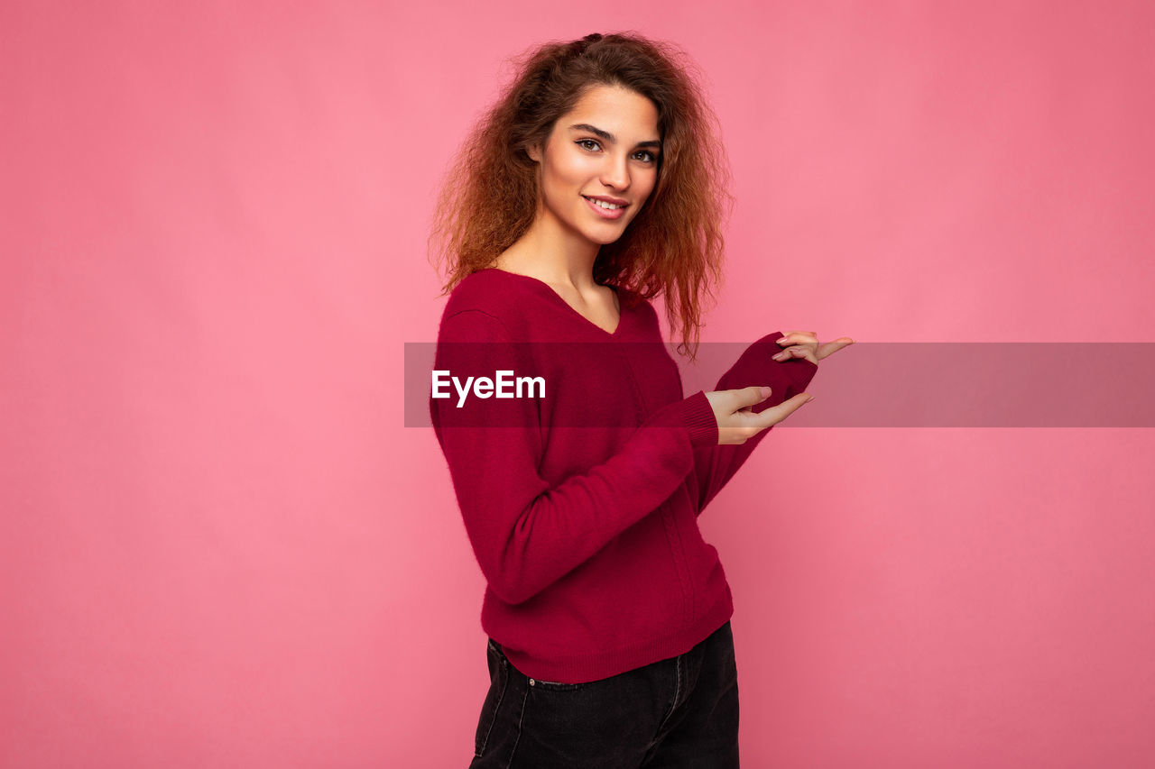 Portrait of smiling young woman against pink background