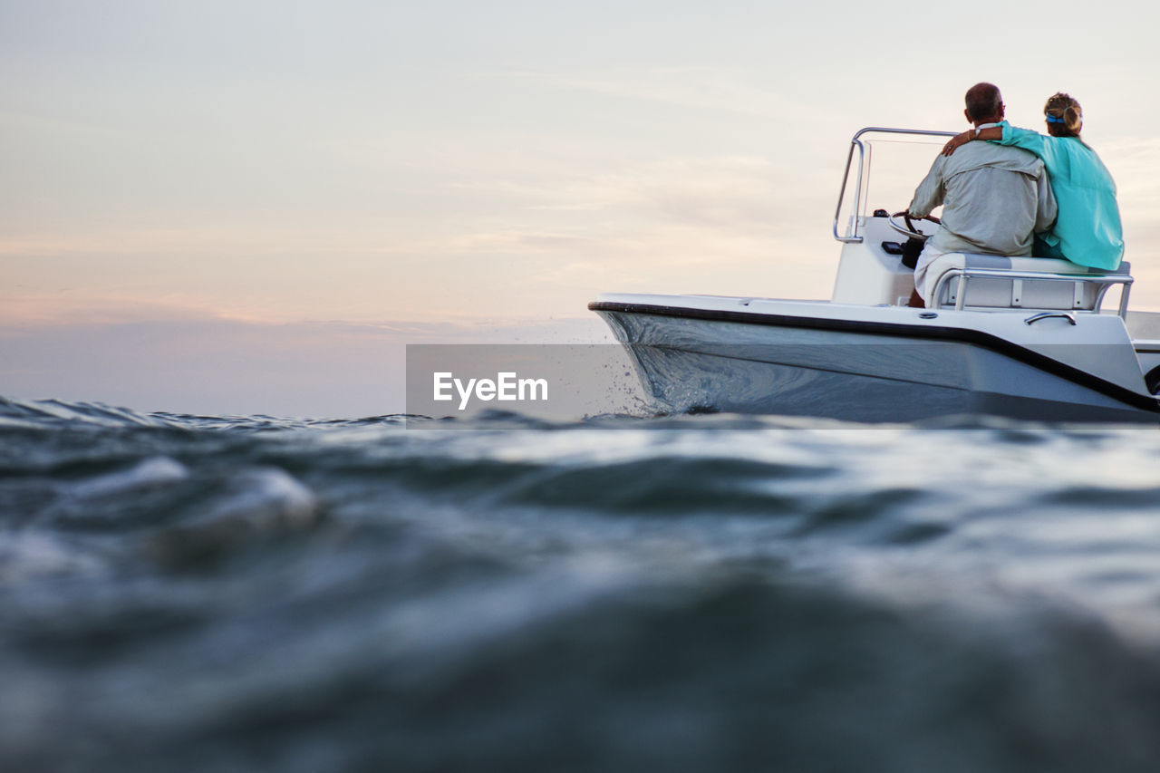 Rear view of couple sitting on boat at sea against sky