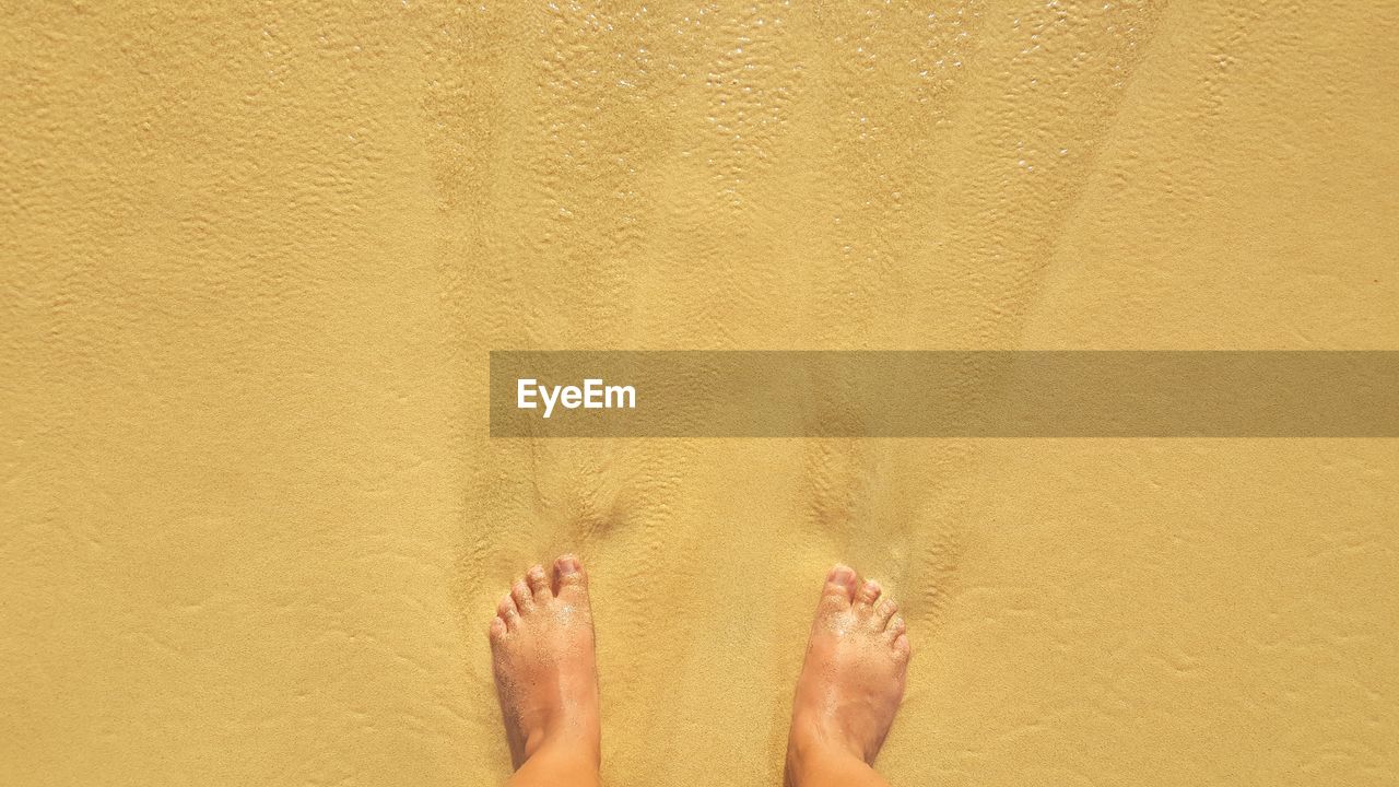 LOW SECTION OF WOMAN FEET ON SAND