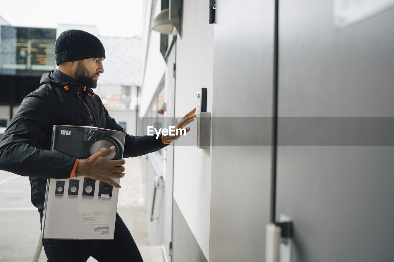 Male worker with box ringing intercom during delivery