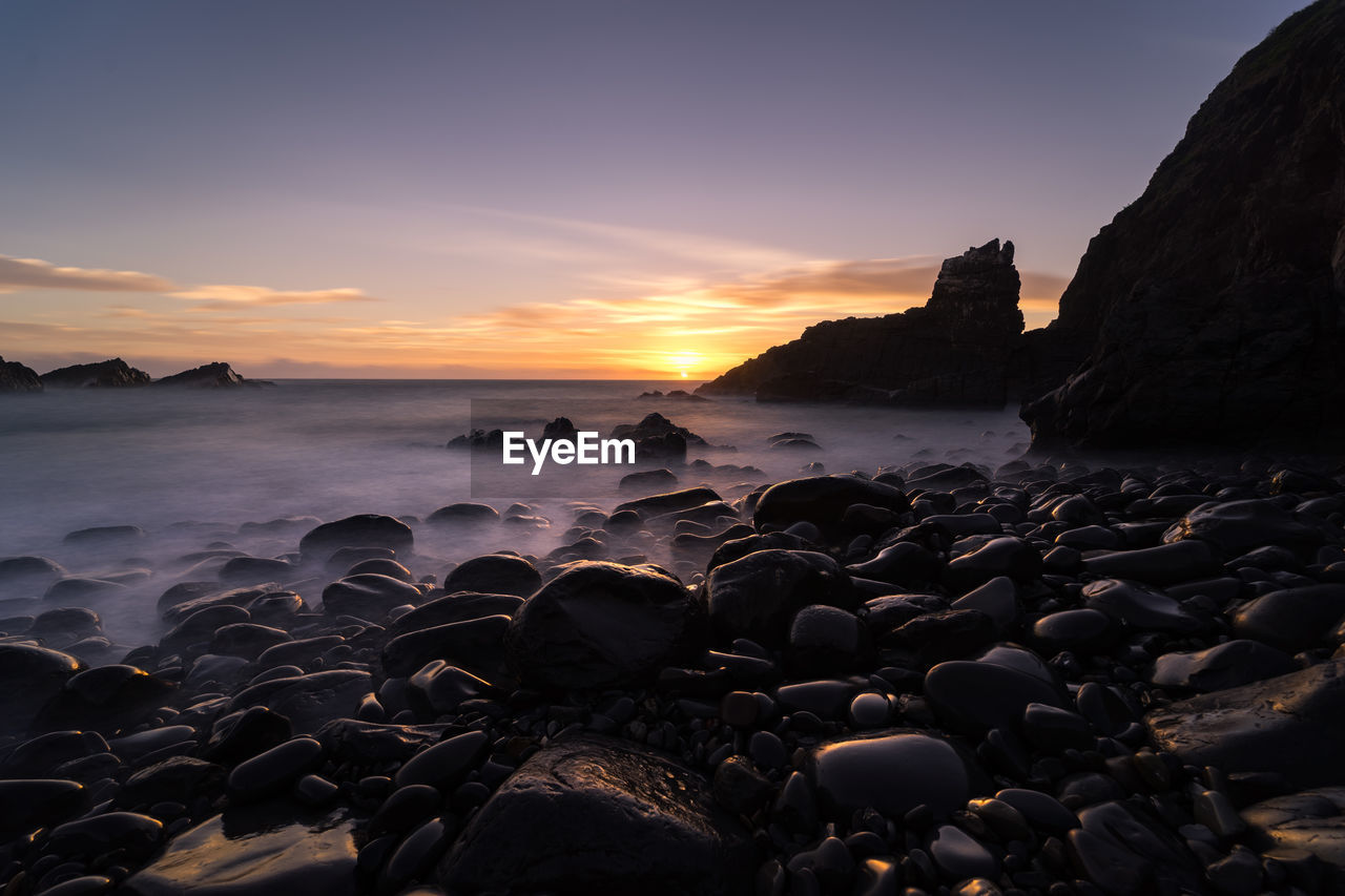 Rocks by sea against sky during sunset