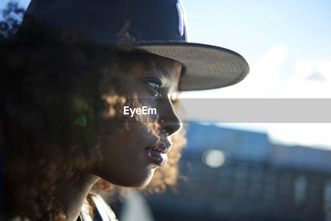 Close-up of woman in cap looking away while standing against sky