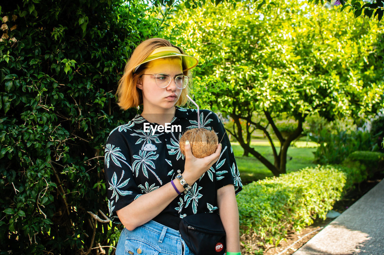 Young woman drinking coconut water with straw while standing in park