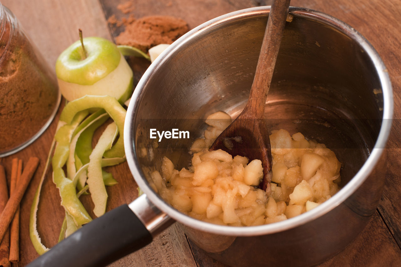 Cooking fresh diced apples to make a sauce with a close up view into the saucepan with wooden spoon