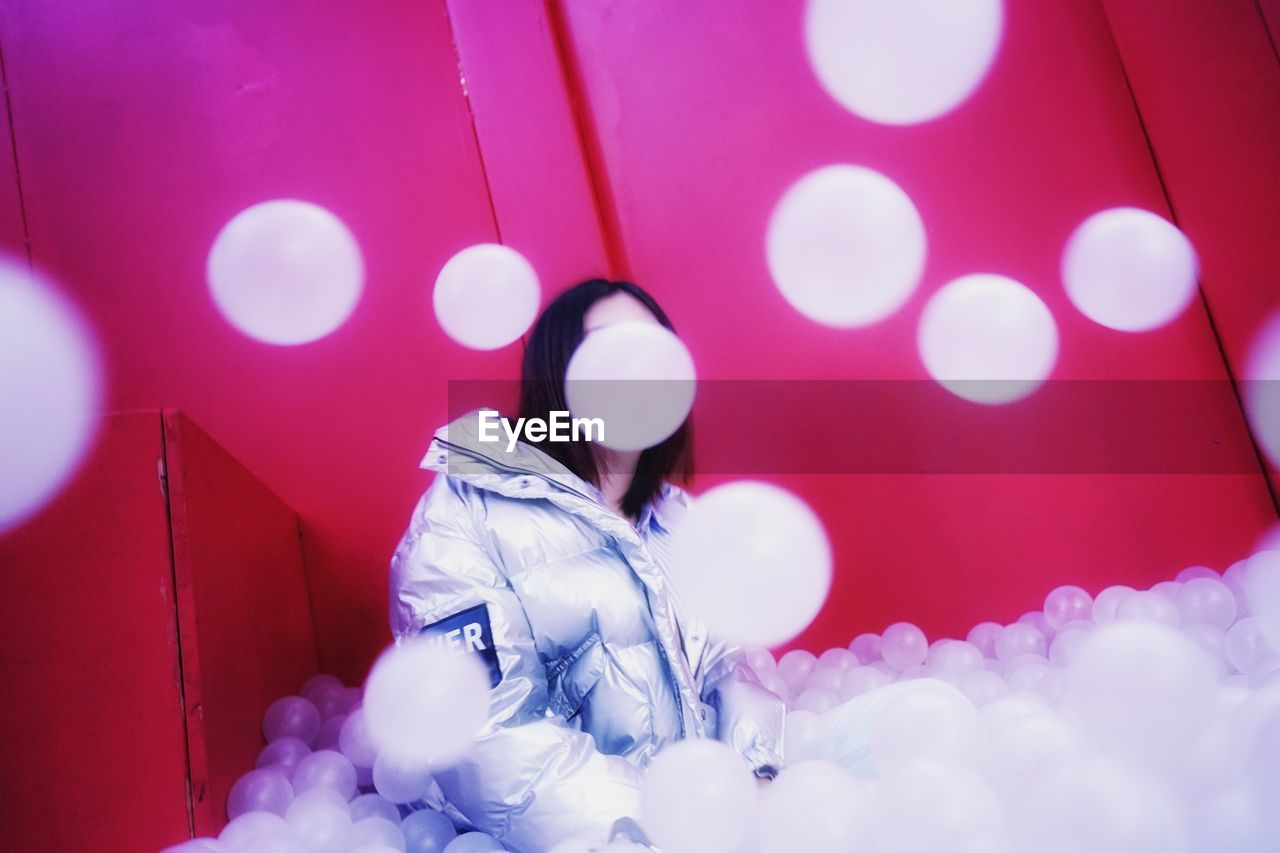 Woman wearing warm clothing sitting amidst balloons seen through window