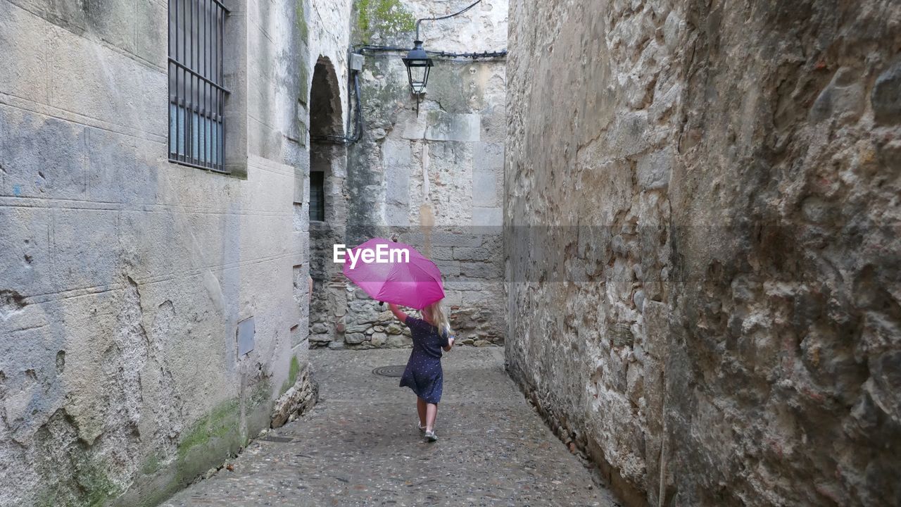 REAR VIEW OF WOMAN WITH PINK UMBRELLA WALKING ON STREET IN CITY