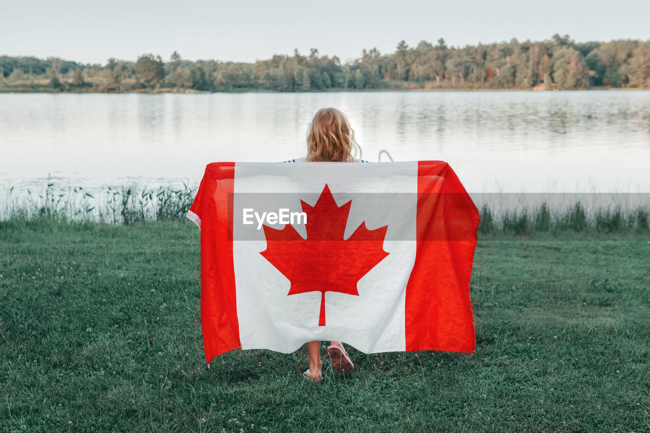 Girl wrapped in large canadian flag by muskoka lake in nature. canada day celebration outdoor. 