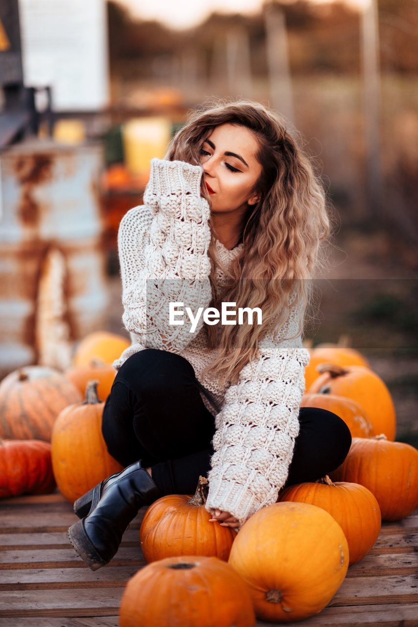 Thoughtful young woman sitting on pumpkins during halloween