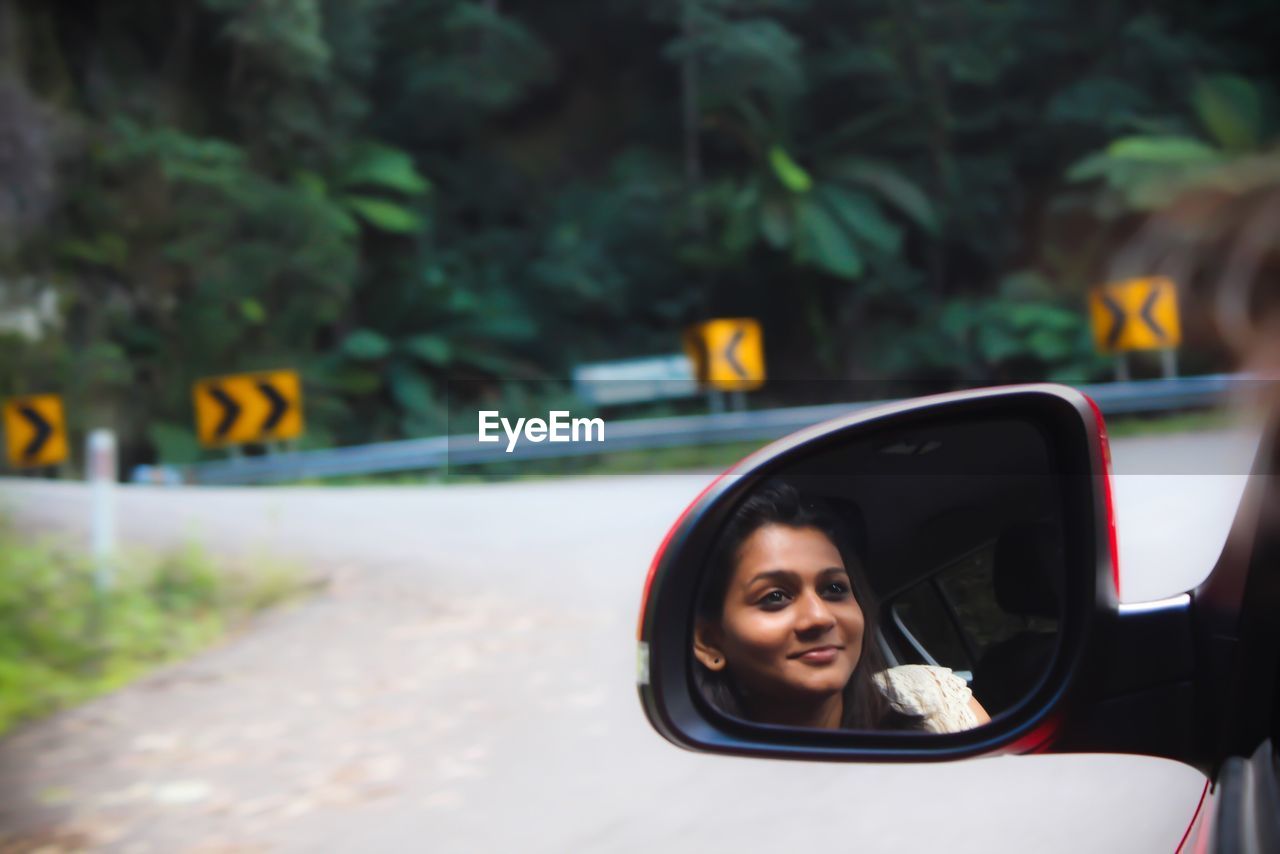 Young woman reflecting on car side-view mirror