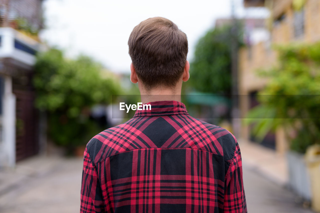 REAR VIEW PORTRAIT OF MAN STANDING AGAINST RED CITY