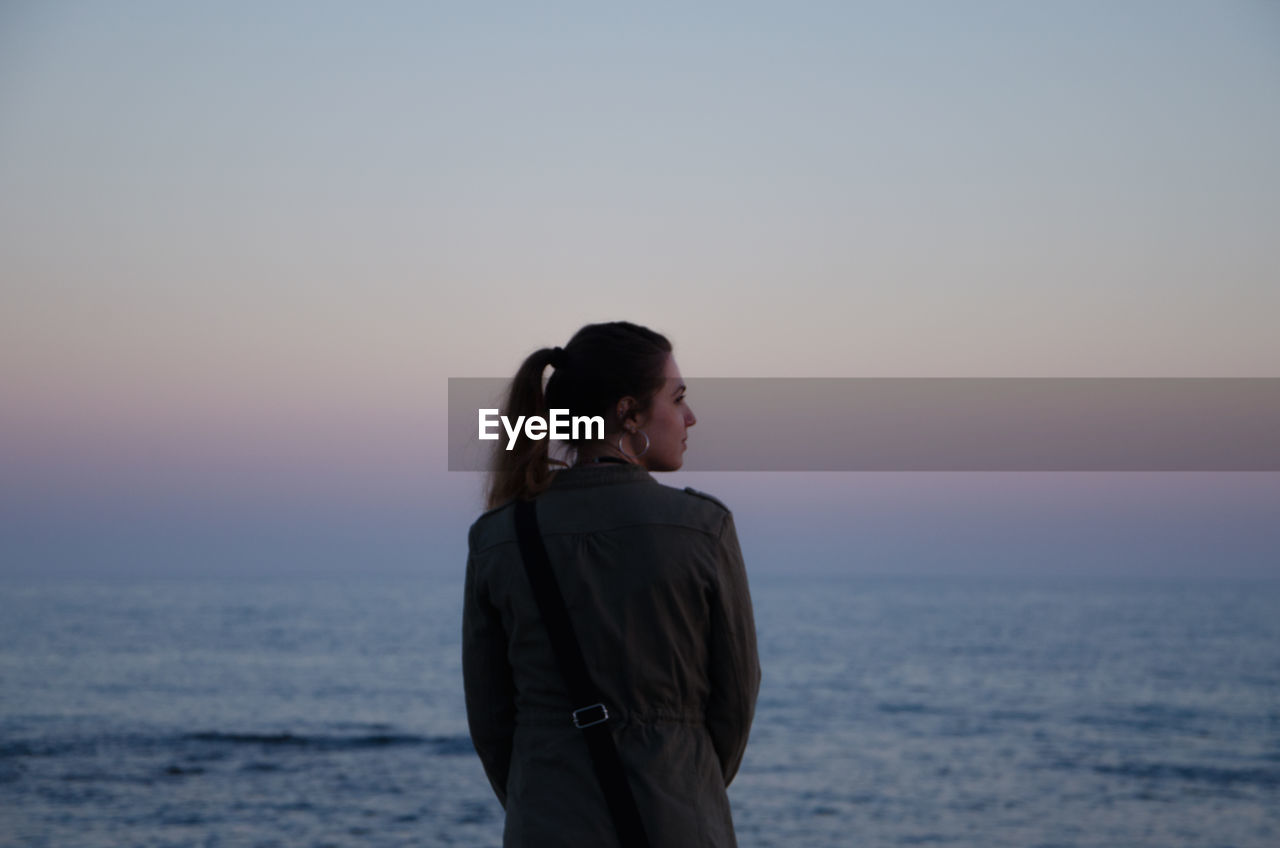 Rear view of woman standing by sea against sky during sunset