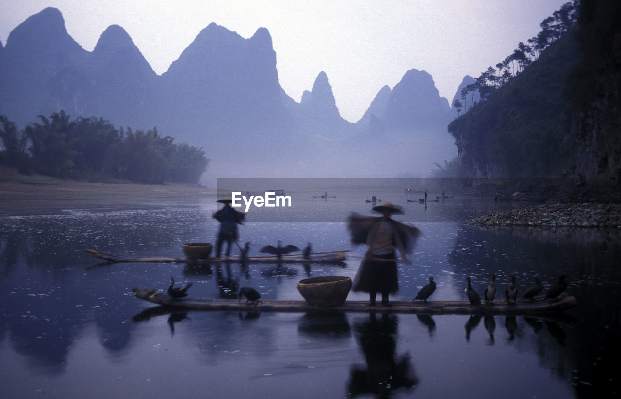 Blurred motion of people on boat in river with reflection against mountains