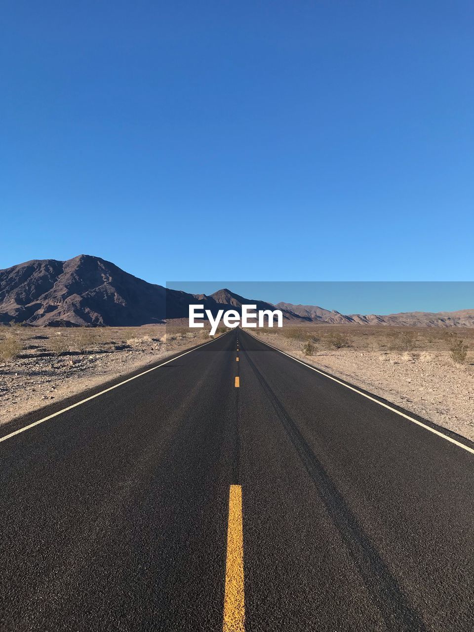 Road leading towards desert against clear blue sky