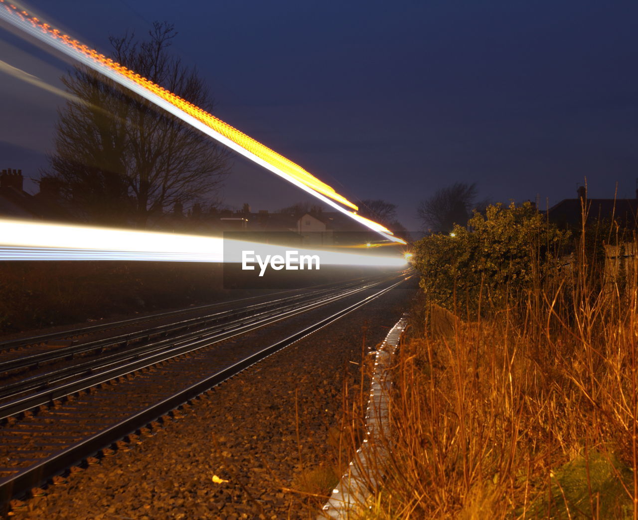 Light trails on railroad tracks against sky at dusk