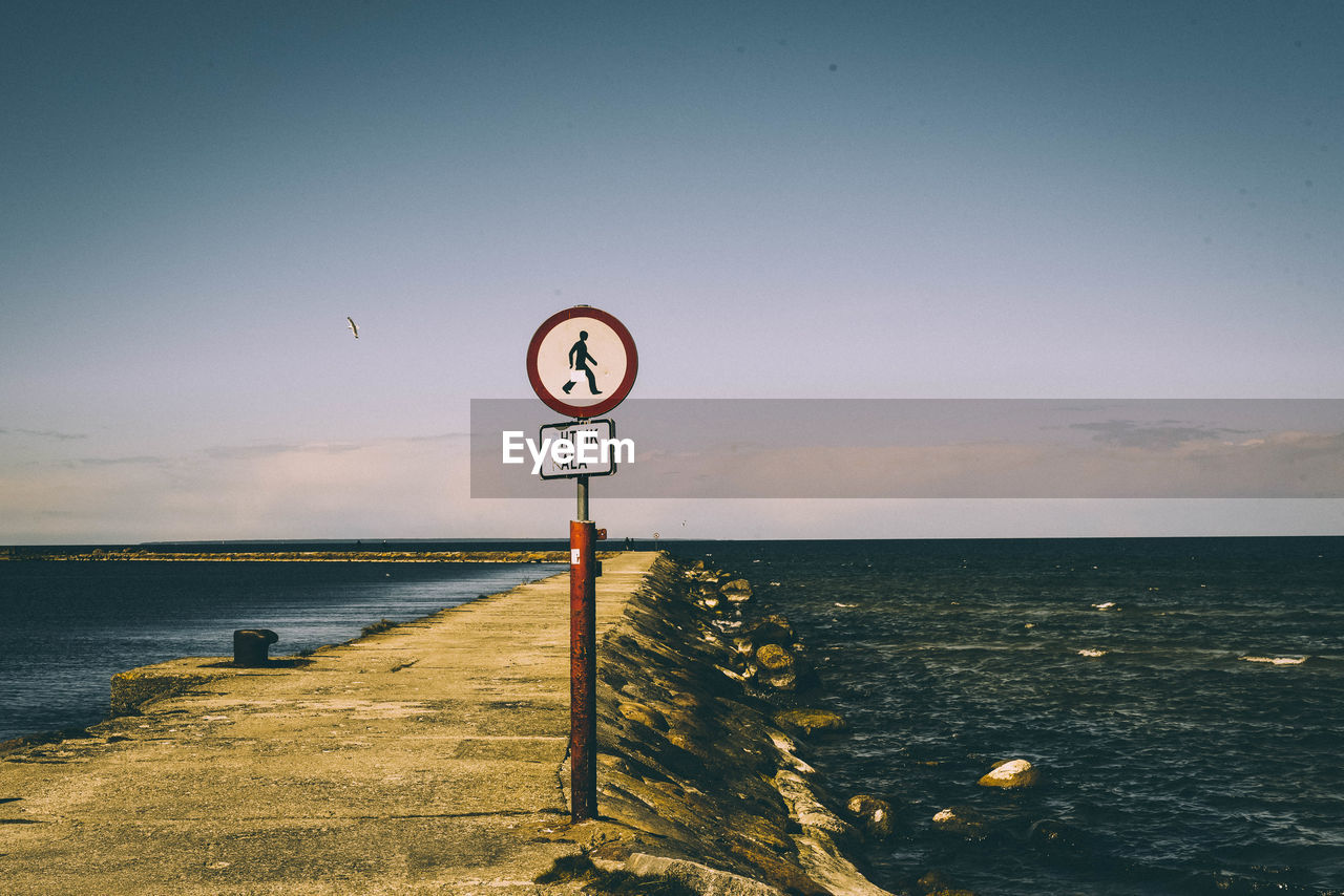 Road sign by sea against clear sky