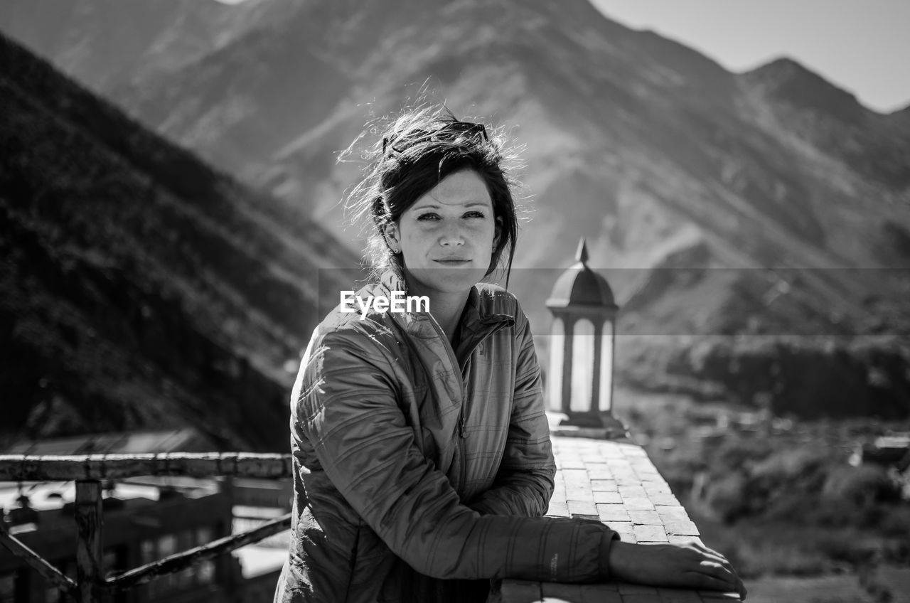 Portrait of woman standing by railing against mountains