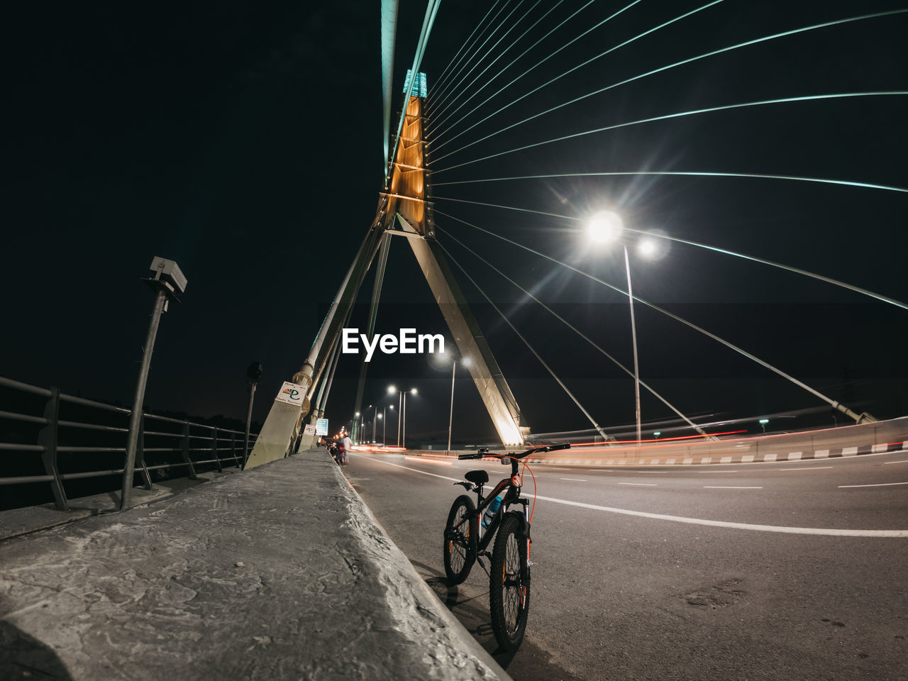 MAN RIDING BICYCLE ON ROAD AGAINST ILLUMINATED CITY AT NIGHT