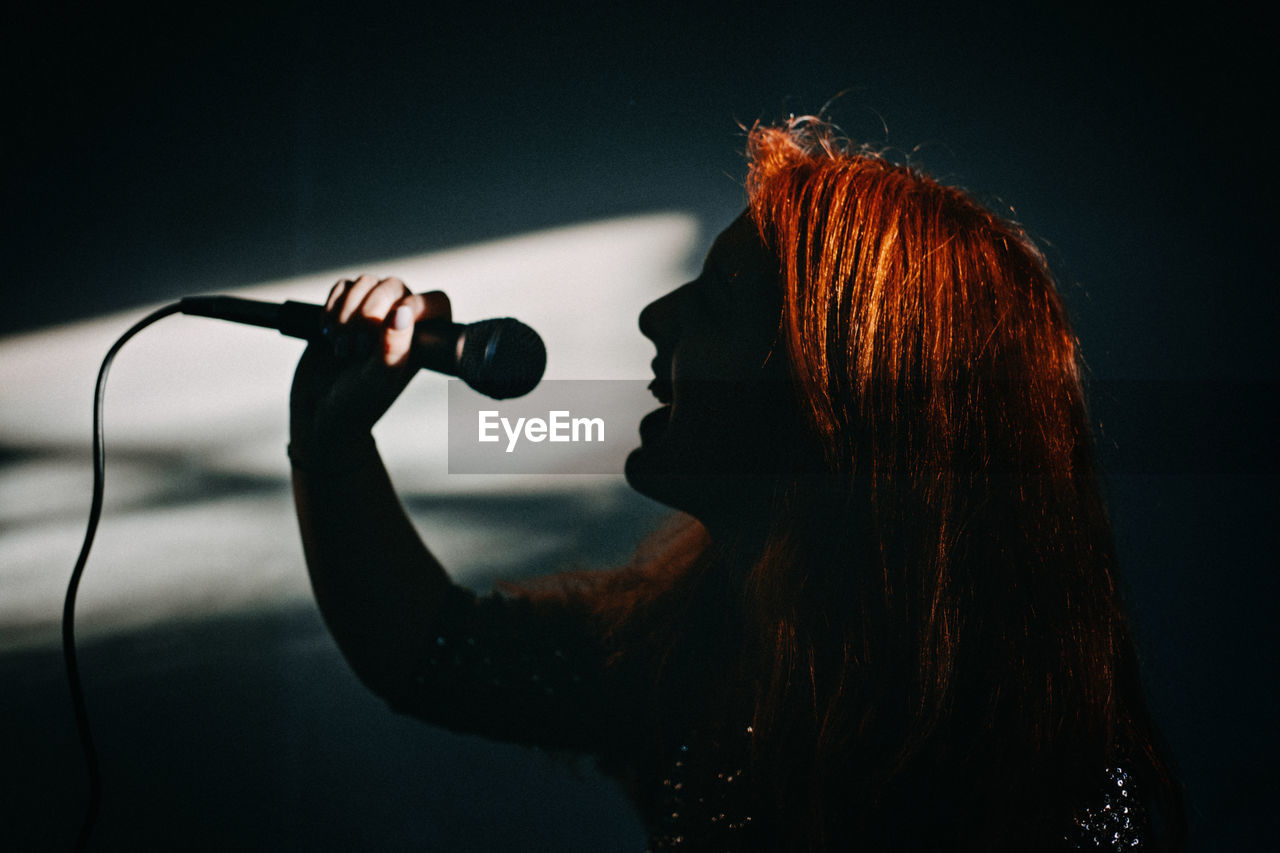 Silhouette, profile of female singer woman holding microphone. excited female singer with modern