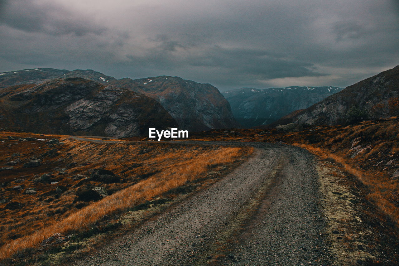 Dirt road by mountains against sky