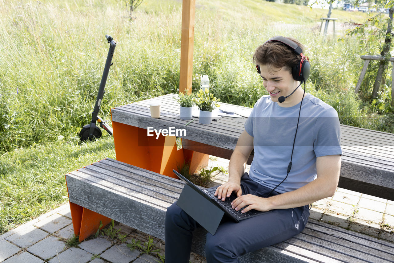 portrait of young man using laptop while sitting on bench