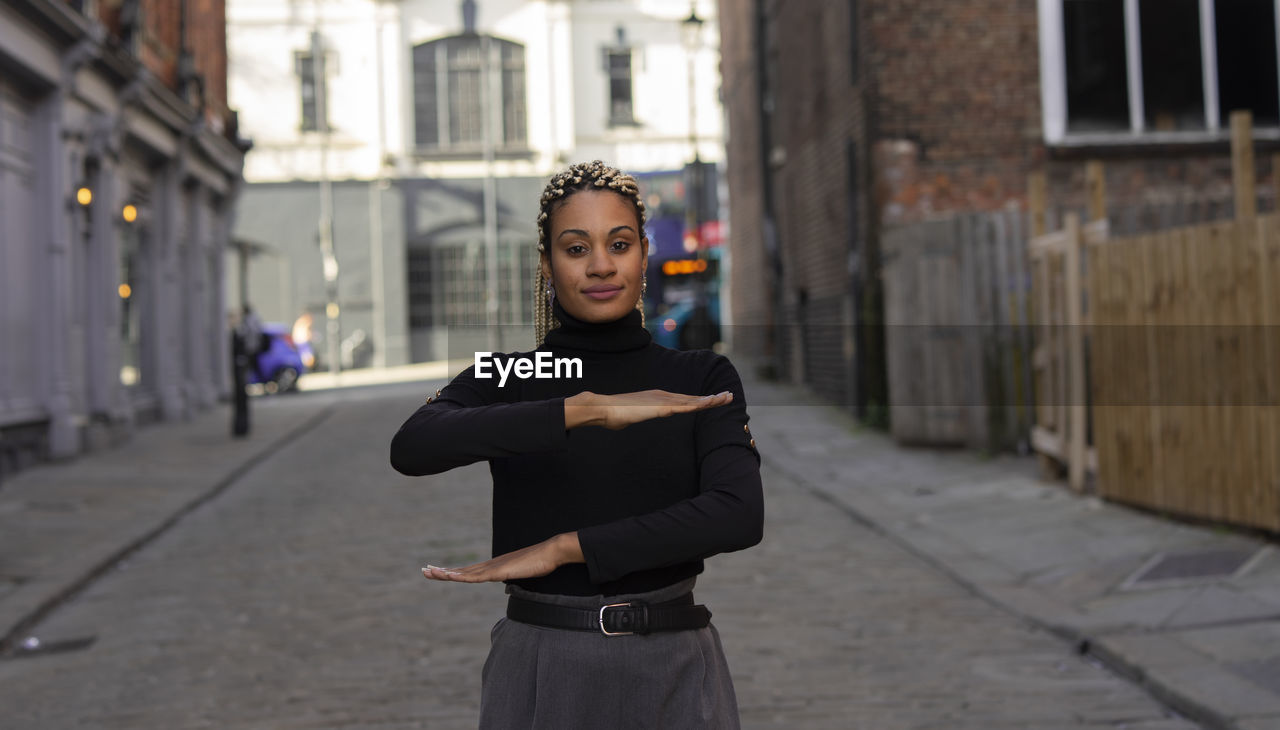 Portrait of woman gesturing while standing on footpath against buildings