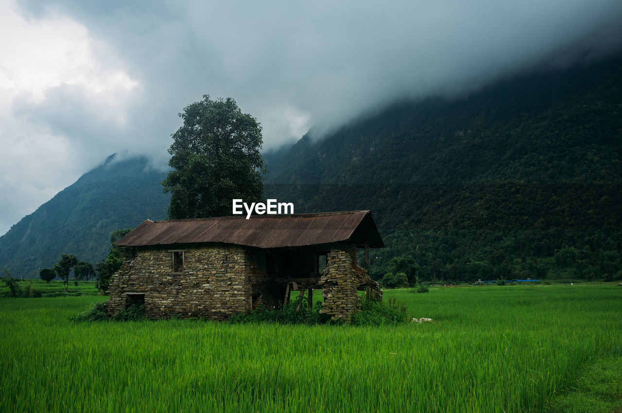 Built house on field by mountain against sky