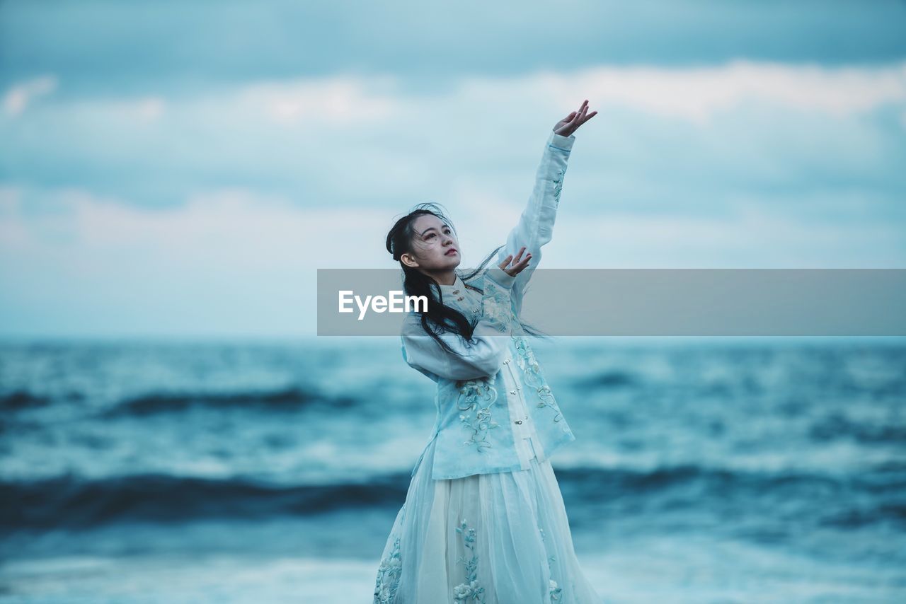 Woman dancing at beach against cloudy sky during sunset