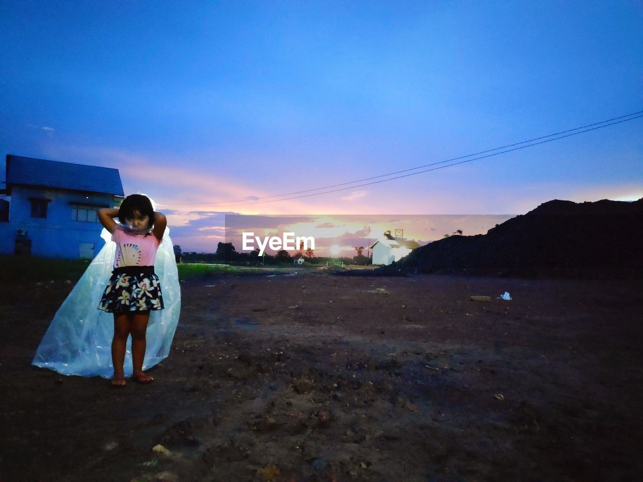 Portrait of girl wearing raincoat while standing on field against cloudy sky during sunset