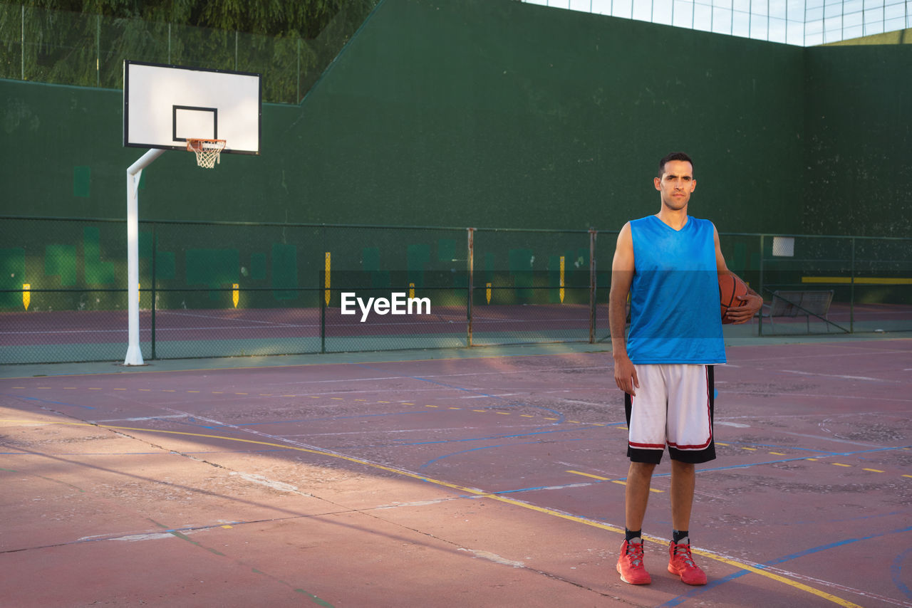 Full length portrait of man standing with basketball in court