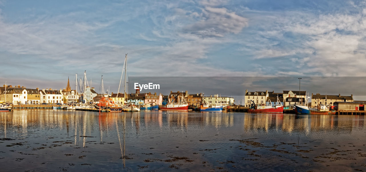 Sailboats in sea by buildings against sky