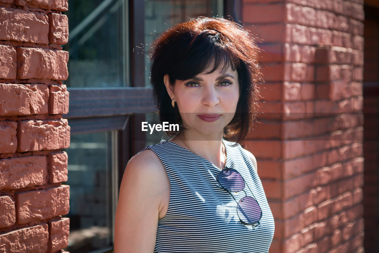 A smiling brunette woman stands in a striped dress outside a red brick building.