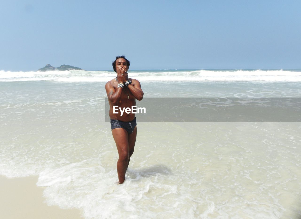 Portrait of shirtless man walking in sea against clear sky