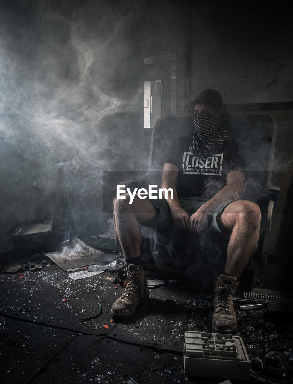 Man sitting on chair with smoke at abandoned home