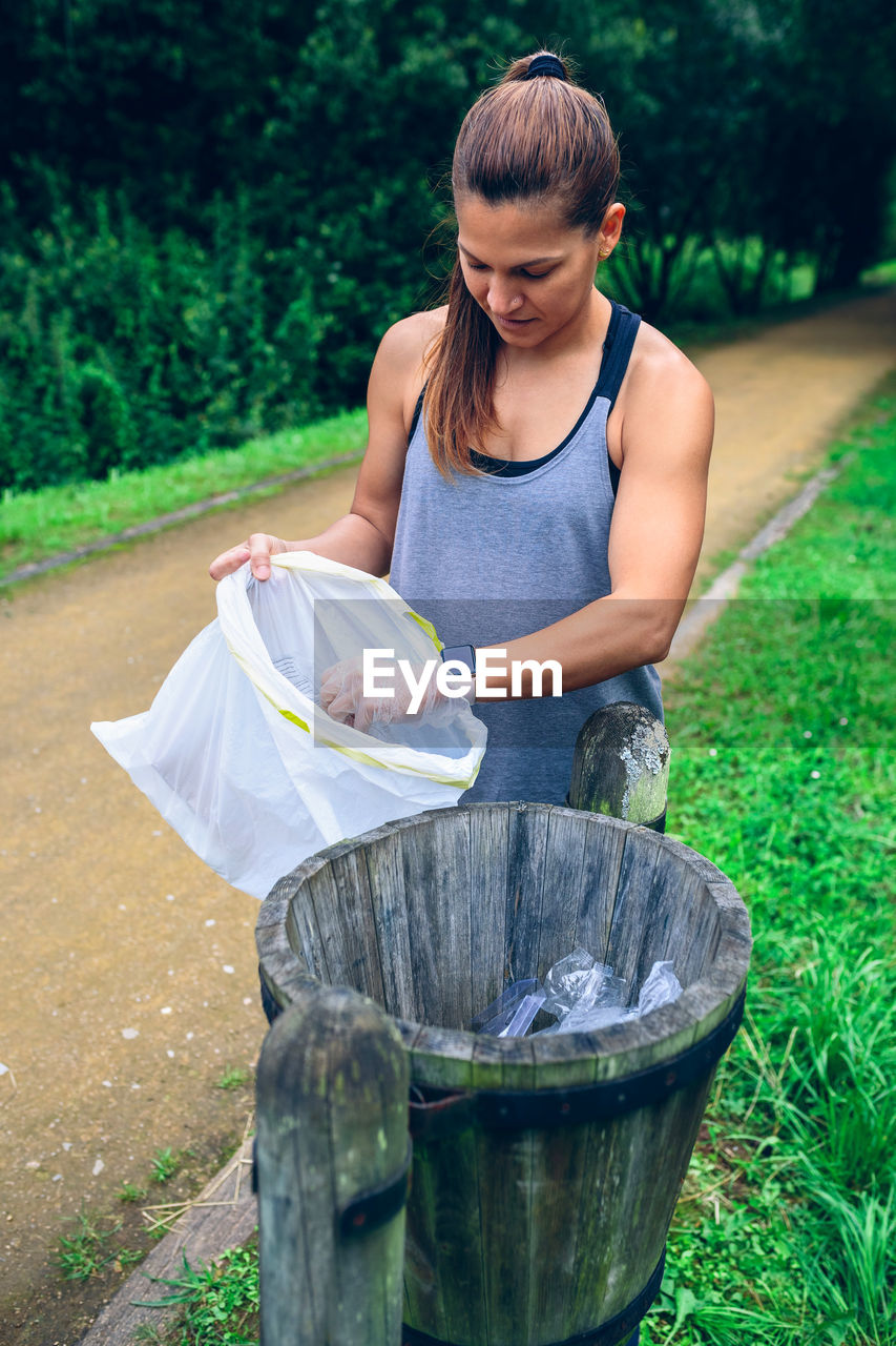 Woman putting garbage in trash can at park