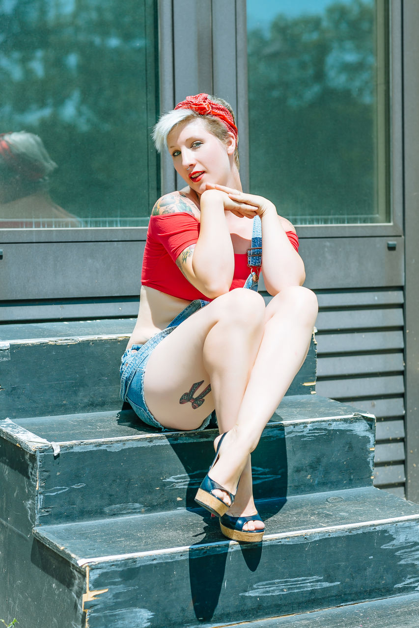 Portrait of beautiful young woman sitting on steps against glass door 