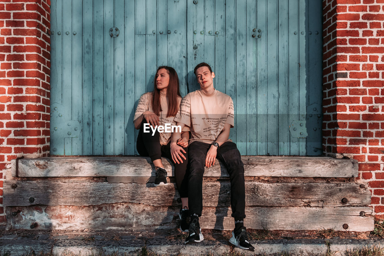 PORTRAIT OF YOUNG COUPLE AGAINST BRICK WALL