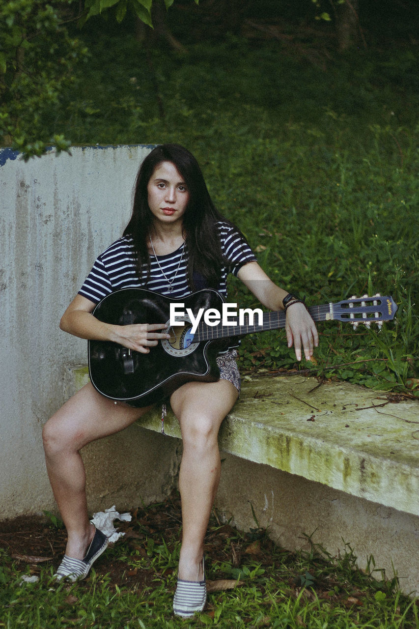 Portrait of young woman with guitar sitting outdoors