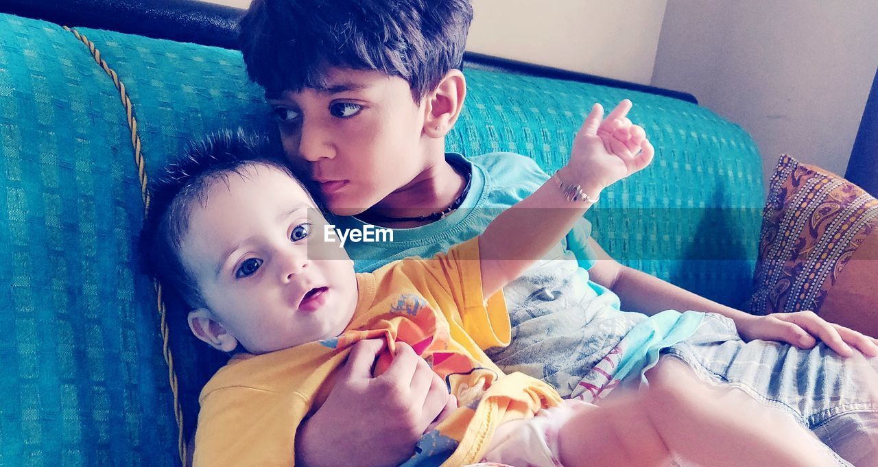 Cute siblings sitting on sofa at home