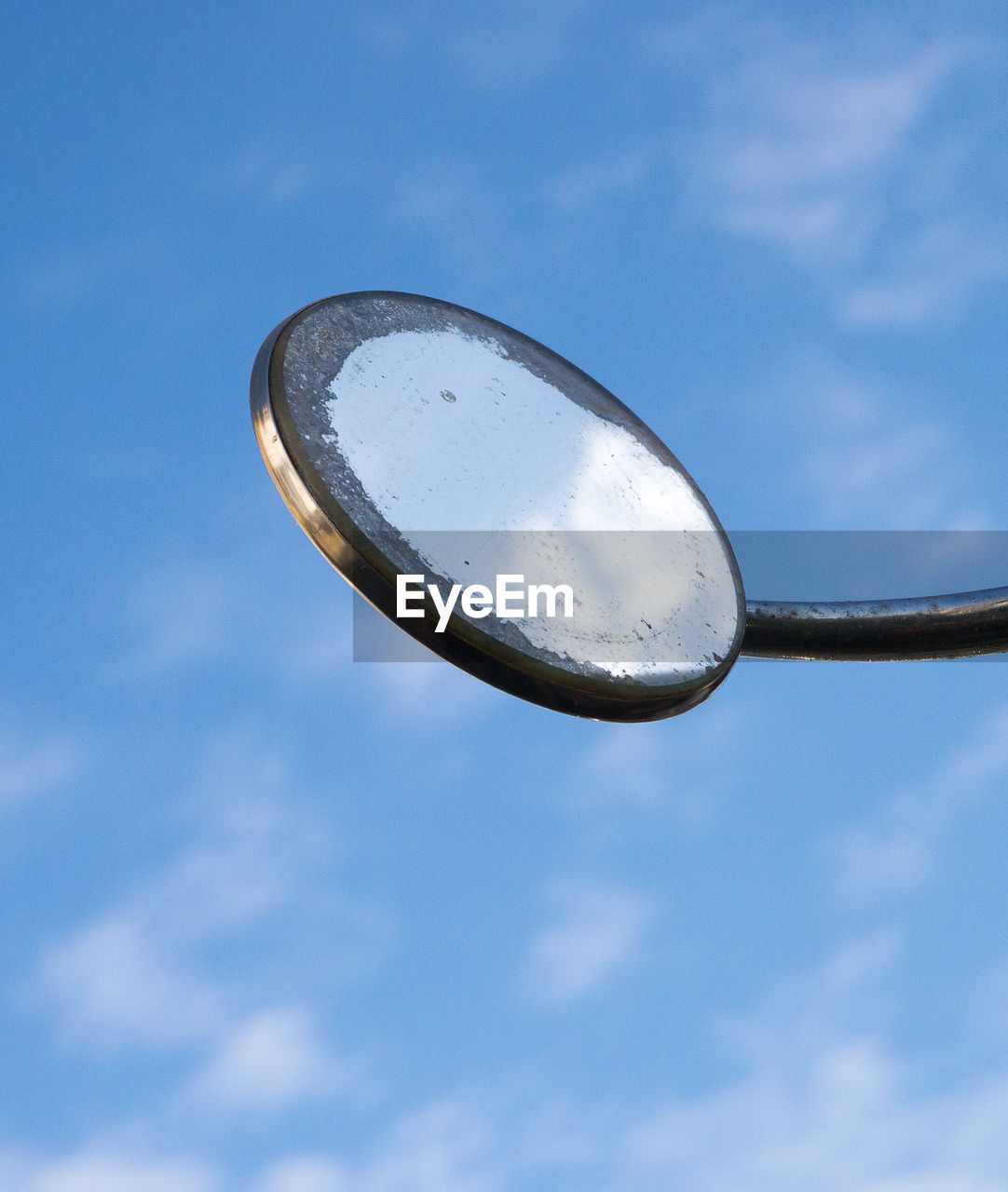 Round mirror of a classic car shot from below against a blue sky