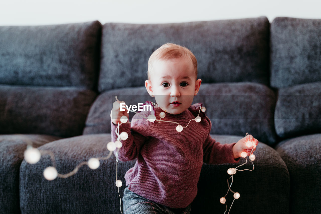 Cute smiling baby girl with decoration sitting on sofa at home