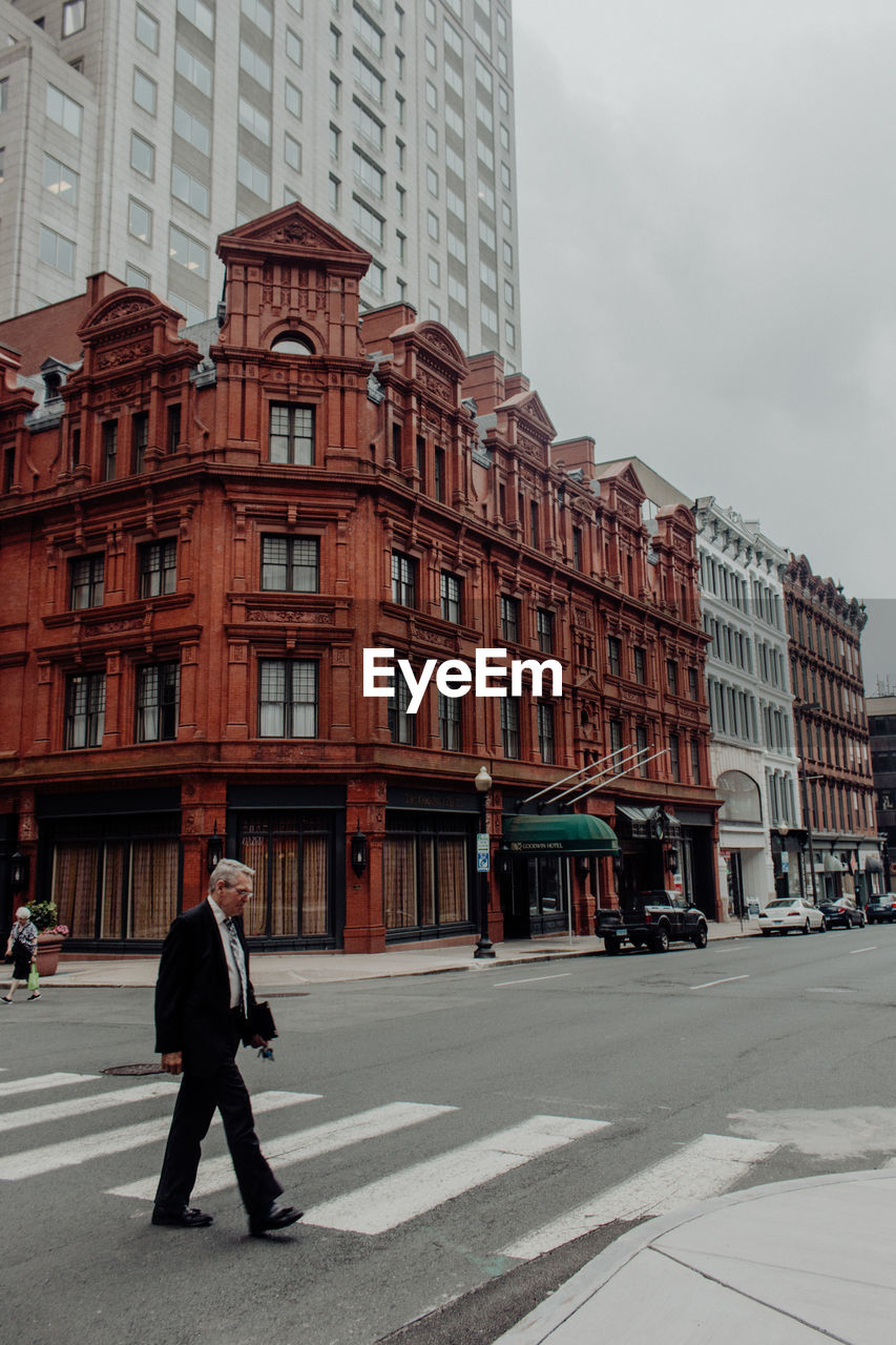 MAN WALKING ON STREET BY BUILDINGS IN CITY