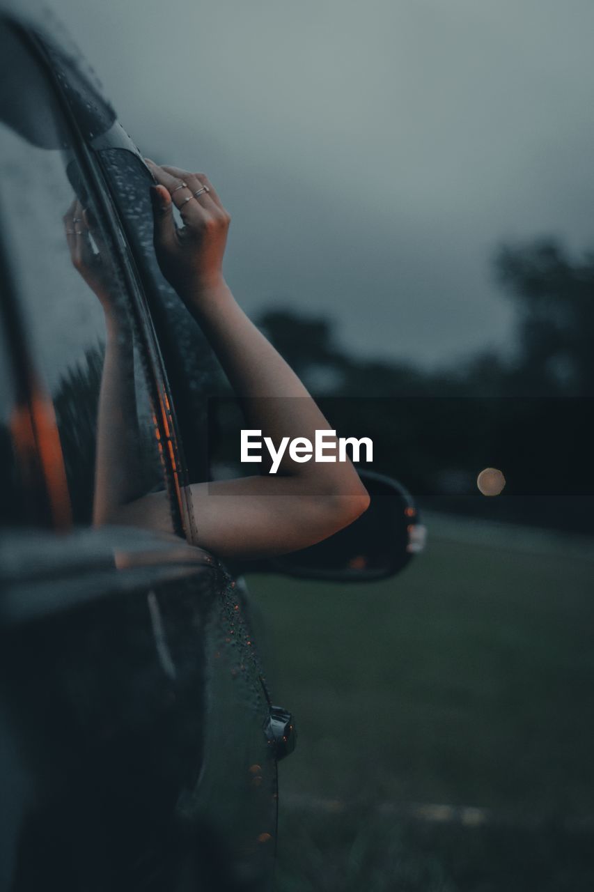 Cropped hand of woman on car against sky at dusk