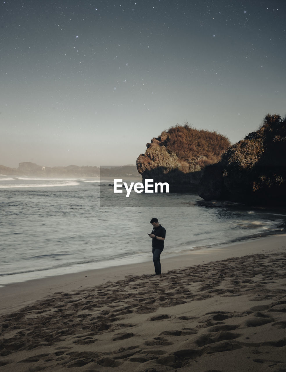 Full length of man using smart phone while standing on beach