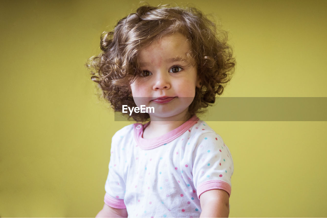 Portrait of cute baby girl standing against yellow background